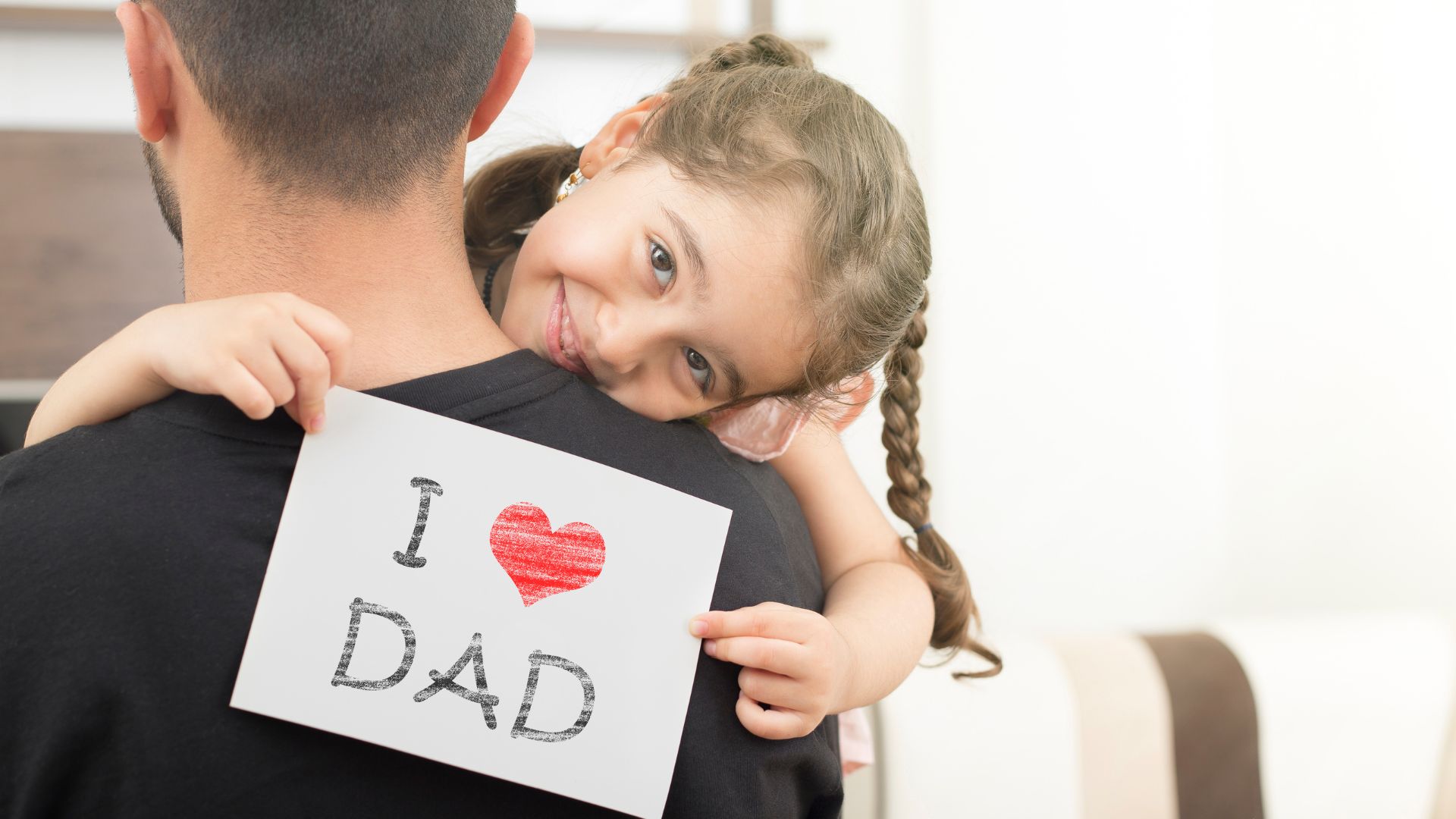 Bambina che abbraccia il papà con un biglietto I love Dad