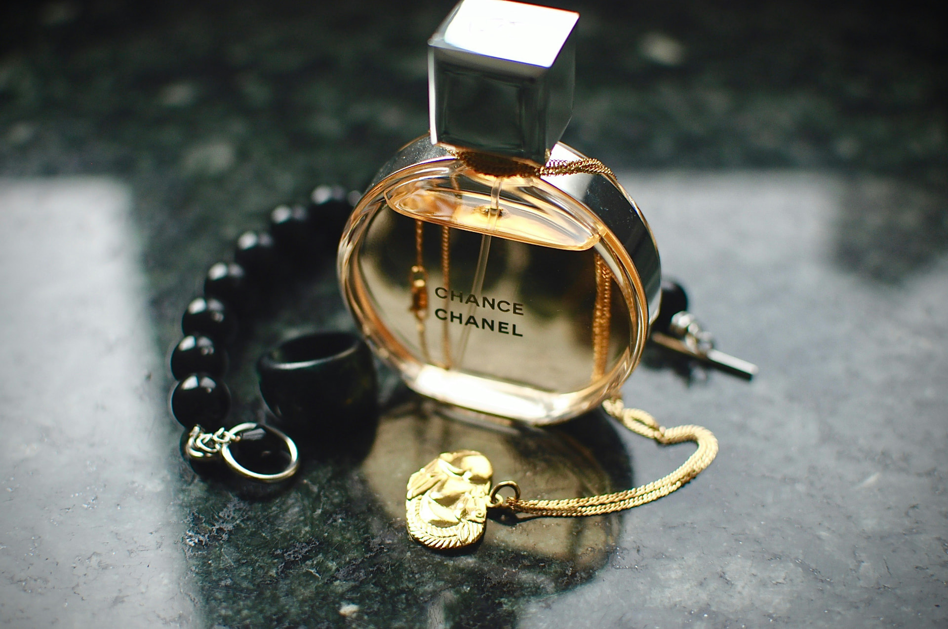 Flacone rotondo Chanel Chance su marmo scuro con gioielli dorati