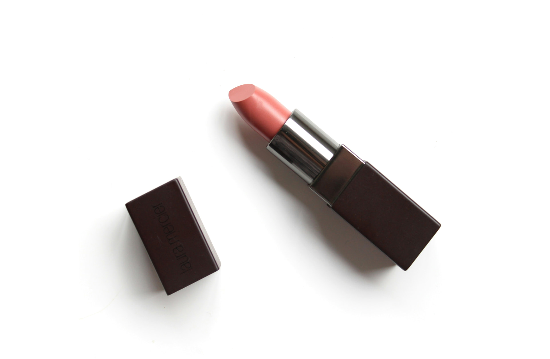 Rossetto rosa nude aperto con tappo accanto su fondo bianco