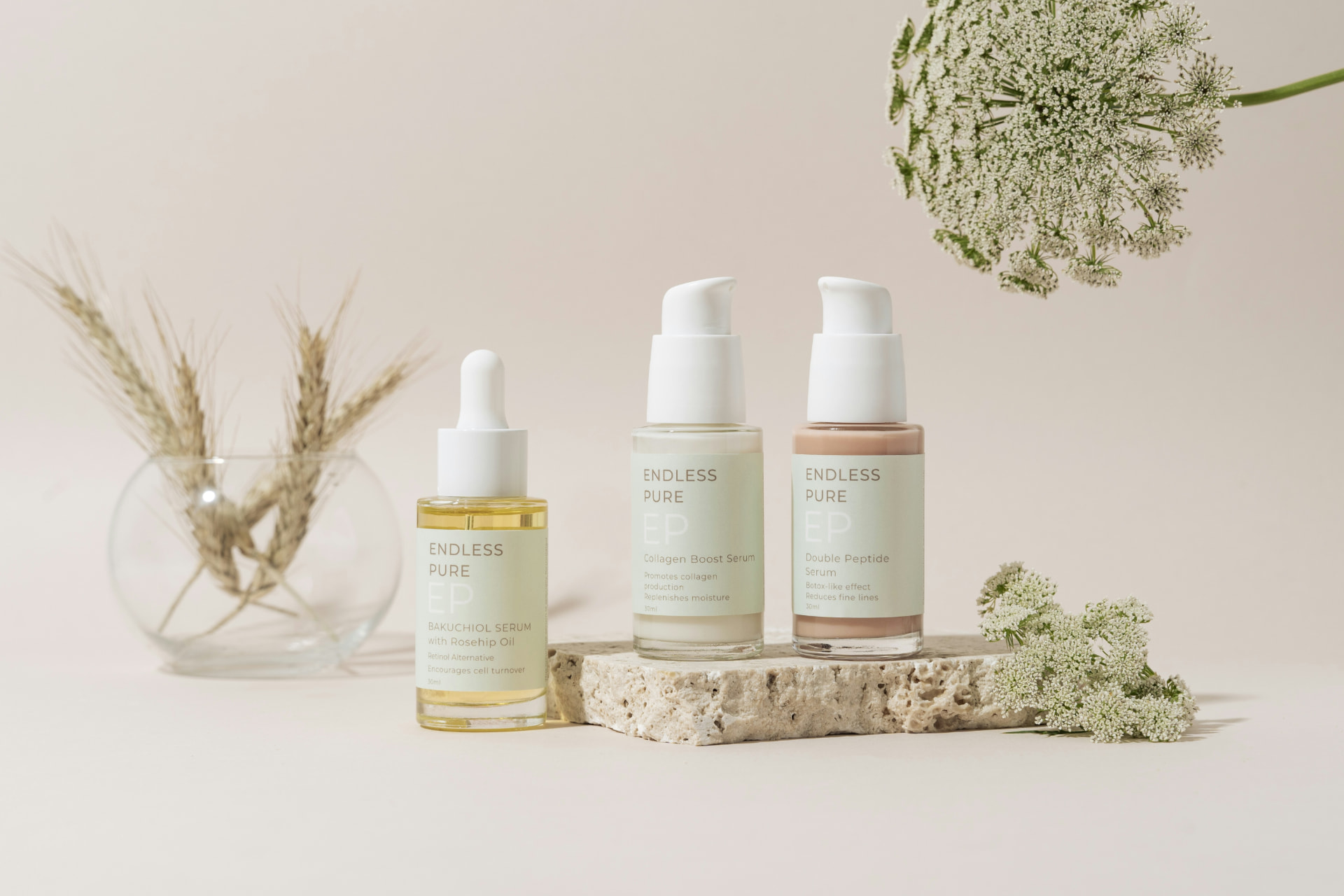 Tre sieri viso al bakuchiol, collagene e peptidi su pietra con spighe e fiori bianchi