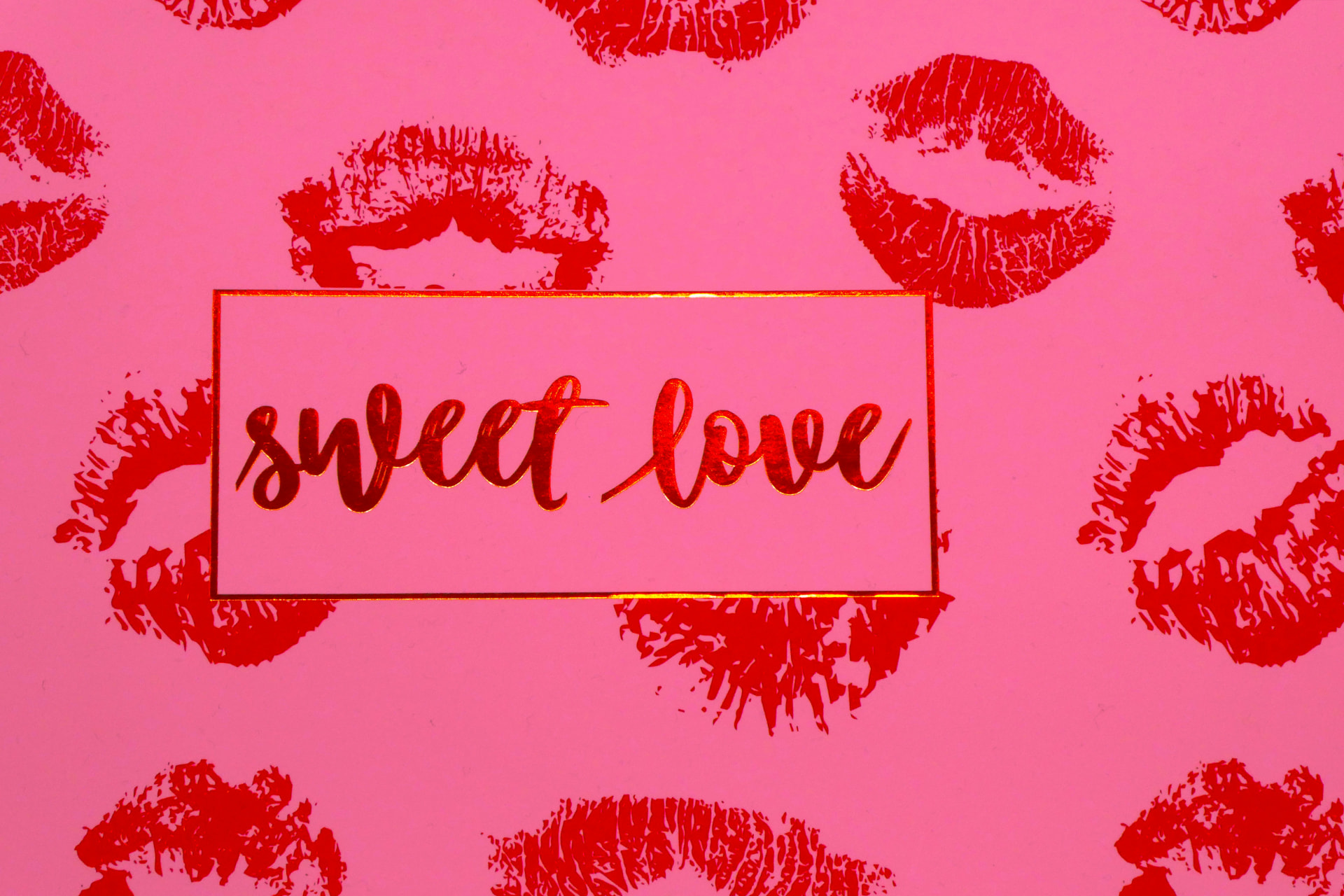 Impronte di rossetto rosso su sfondo rosa con scritta sweet love per il trucco di San Valentino