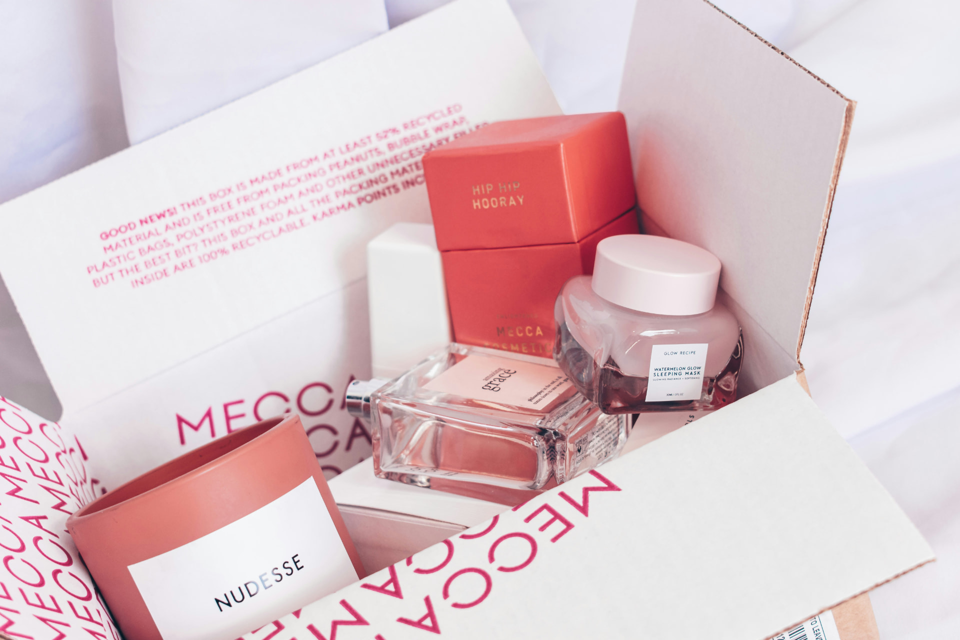 Cofanetto regalo beauty aperto con flacone di profumo femminile, candela e maschera viso su tessuto bianco