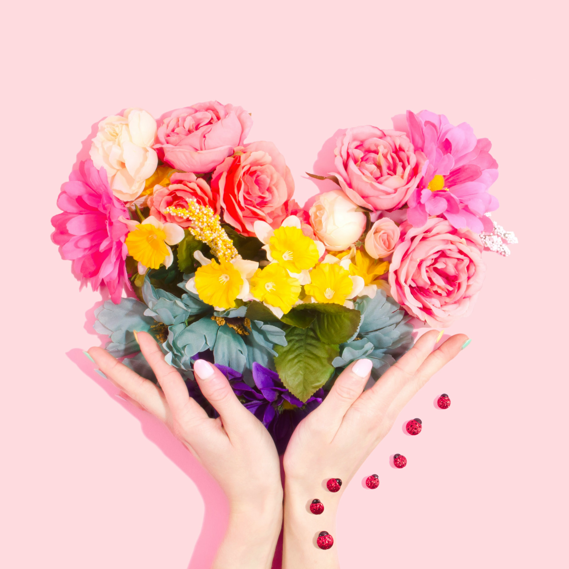 Mani che sorreggono un bouquet di fiori a forma di cuore su sfondo rosa, idea regalo per San Valentino