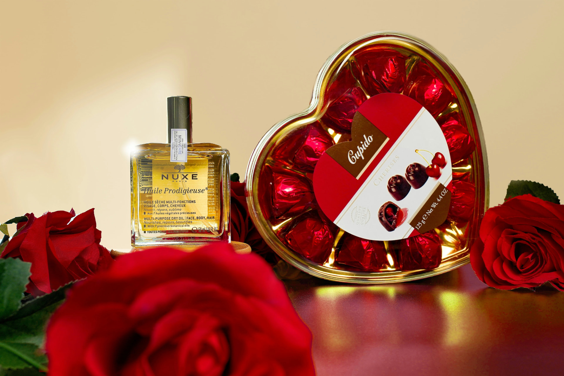 Flacone di olio profumato tra rose rosse e scatola di cioccolatini a cuore per San Valentino