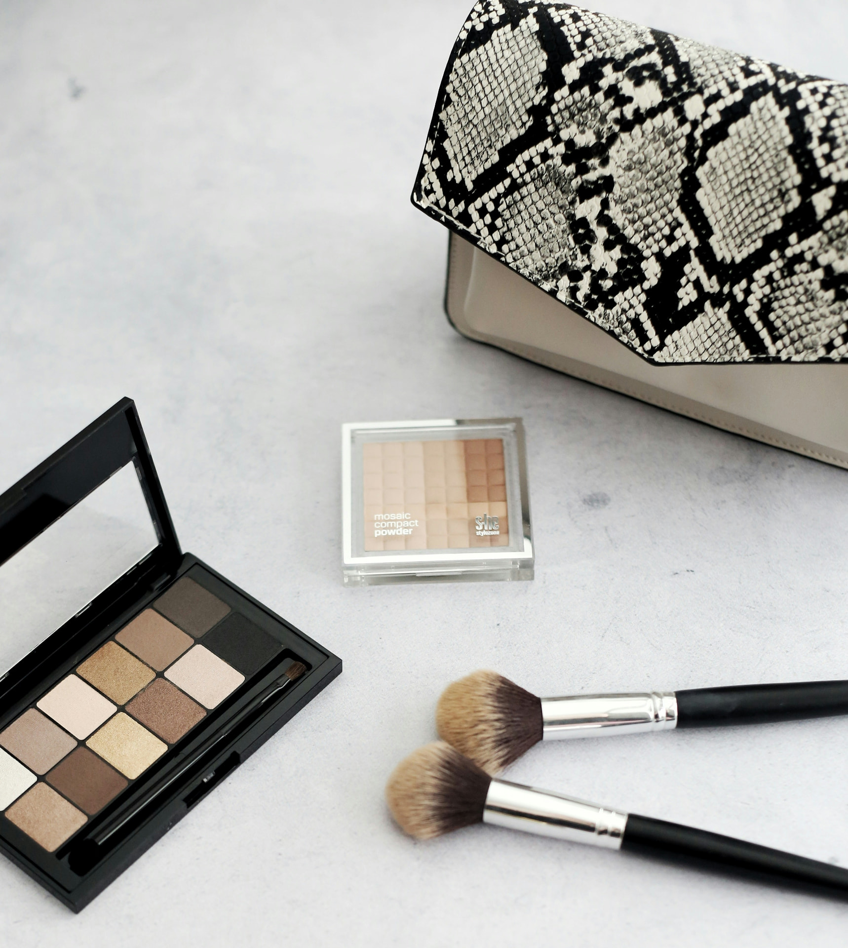 Palette di ombretti nude con cipria compatta e pennelli da trucco su fondo chiaro