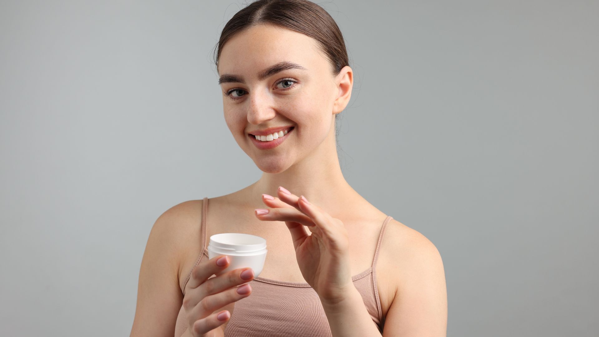 Donna sorridente che tiene un vasetto di crema viso