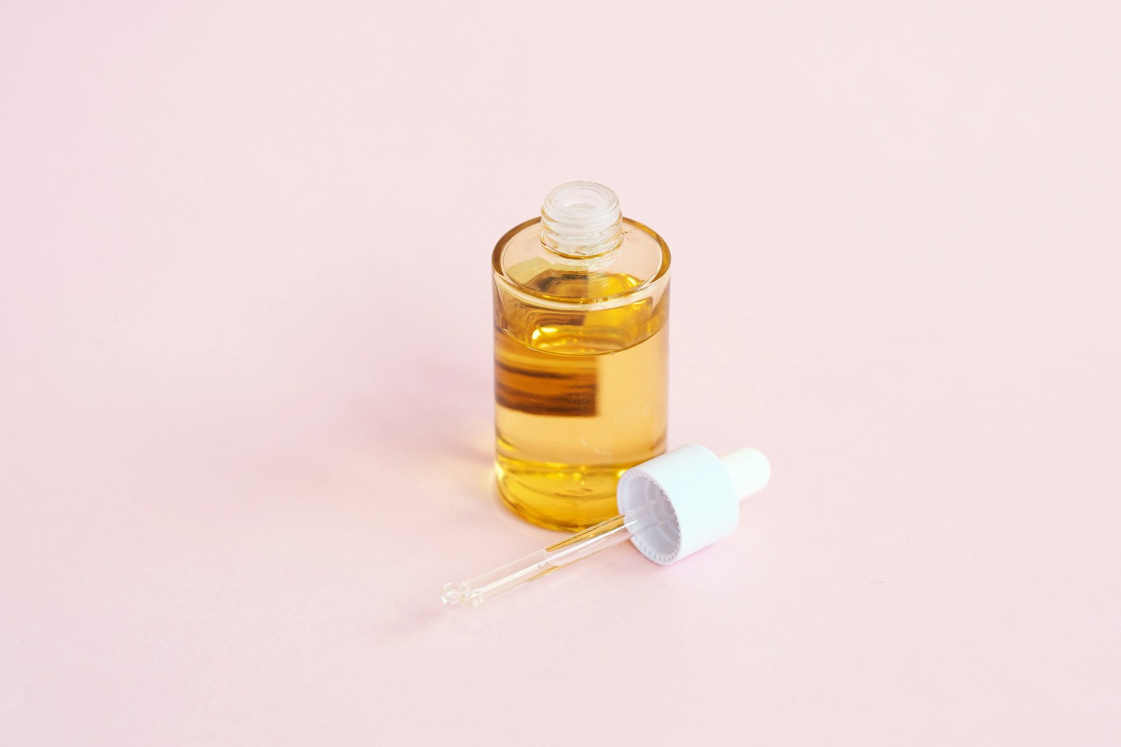 Flacone di siero viso con pipetta su superficie rosa minimalista