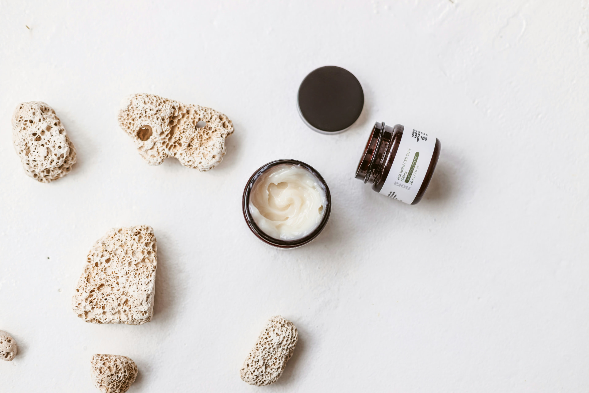 Vasetti aperti di crema detergente viso con pietre naturali su fondo bianco
