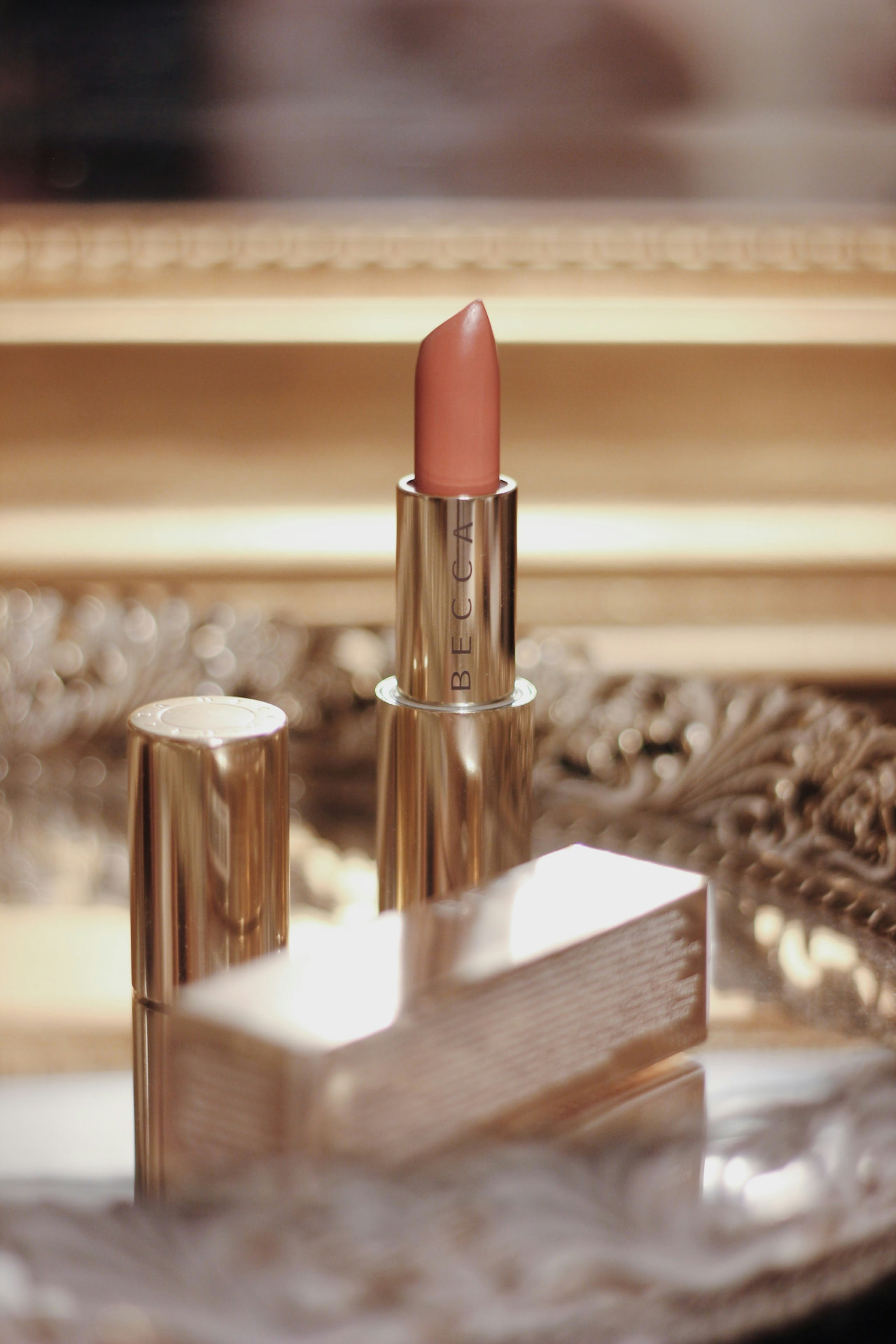 Rossetto nude in astuccio dorato davanti a una cornice dorata