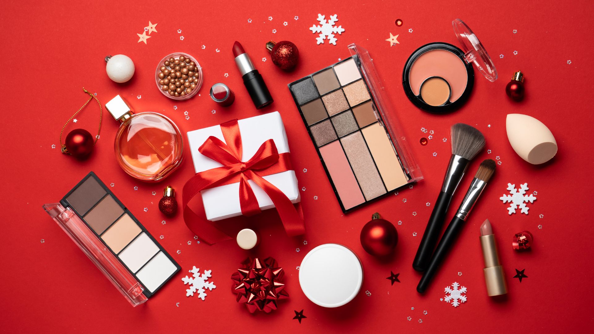 Prodotti make-up per Natale su fondo rosso con decorazioni festive