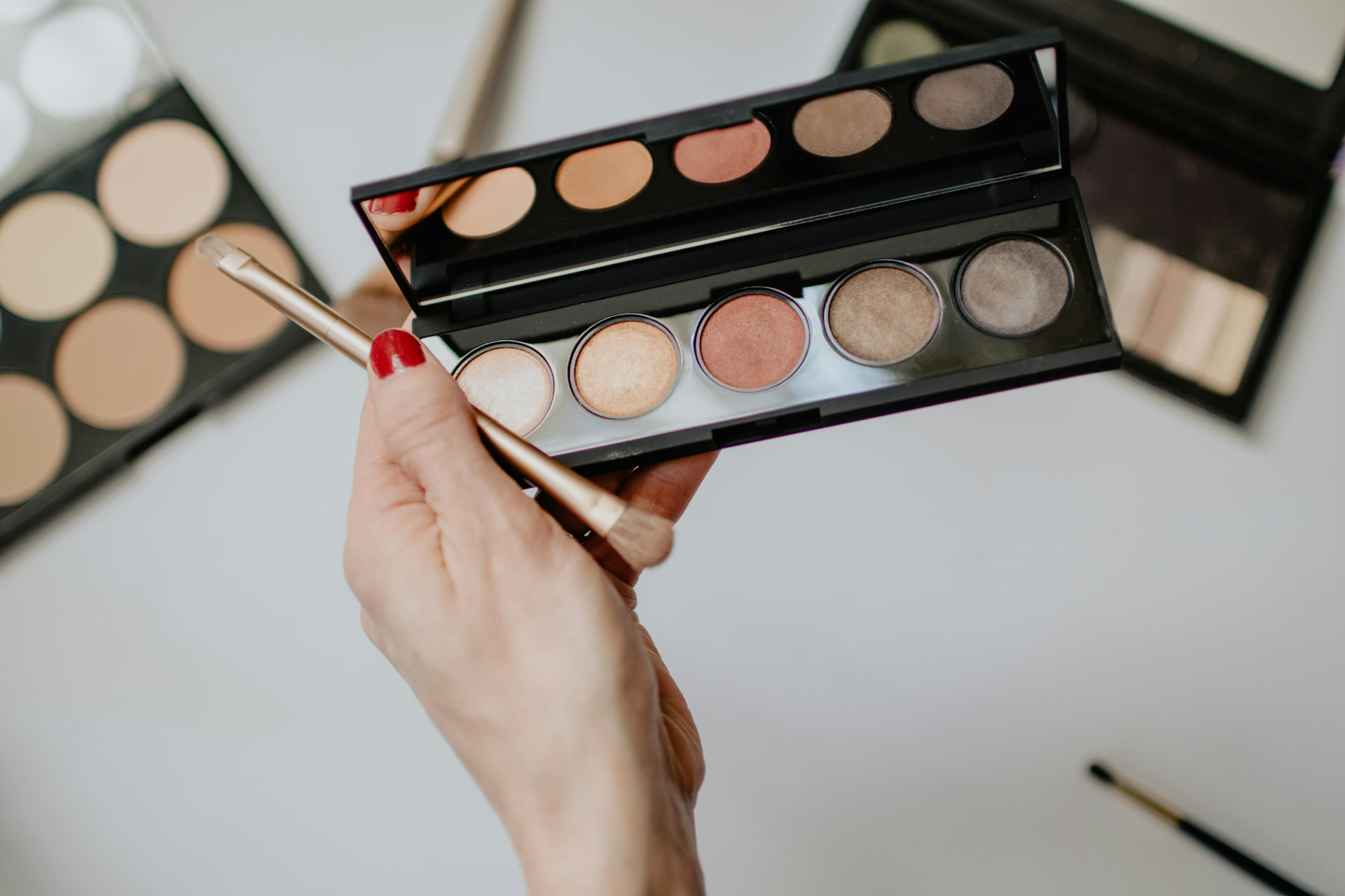 Palette di ombretti shimmer tenuta in mano con pennello dorato