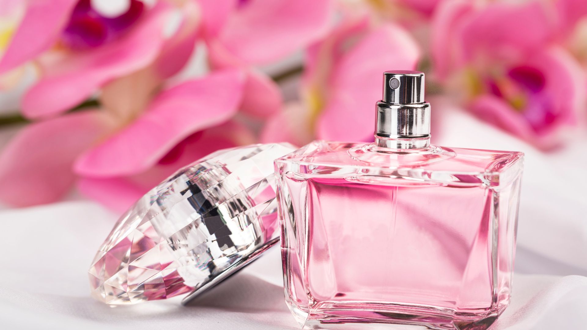 Flacone di profumo rosa tra fiori di orchidea