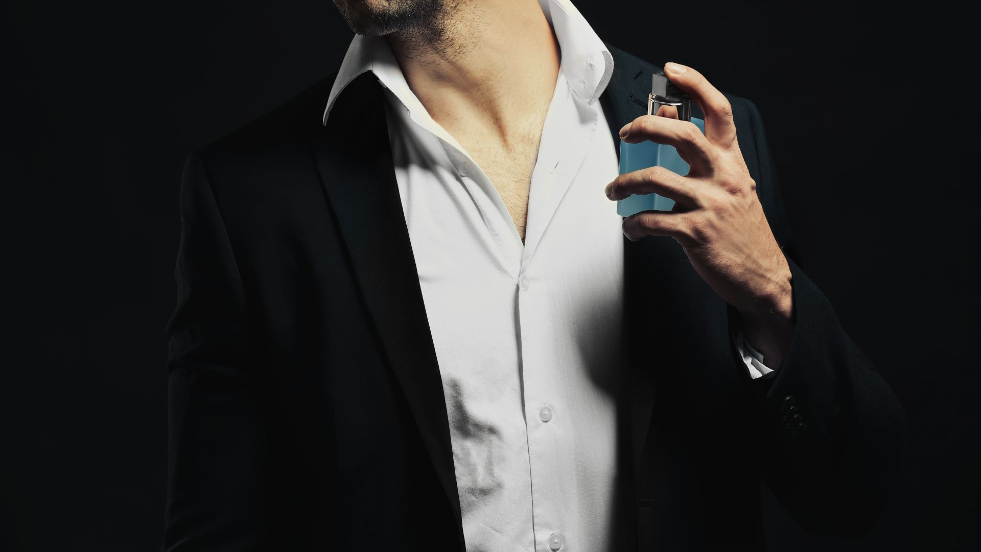 Uomo in giacca scura che vaporizza il profumo
