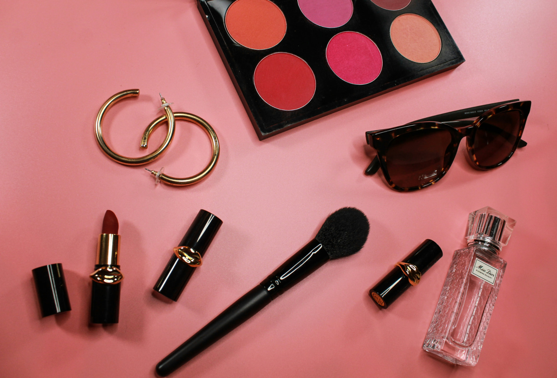 Palette di blush colorati con pennello, rossetti e profumo su fondo rosa