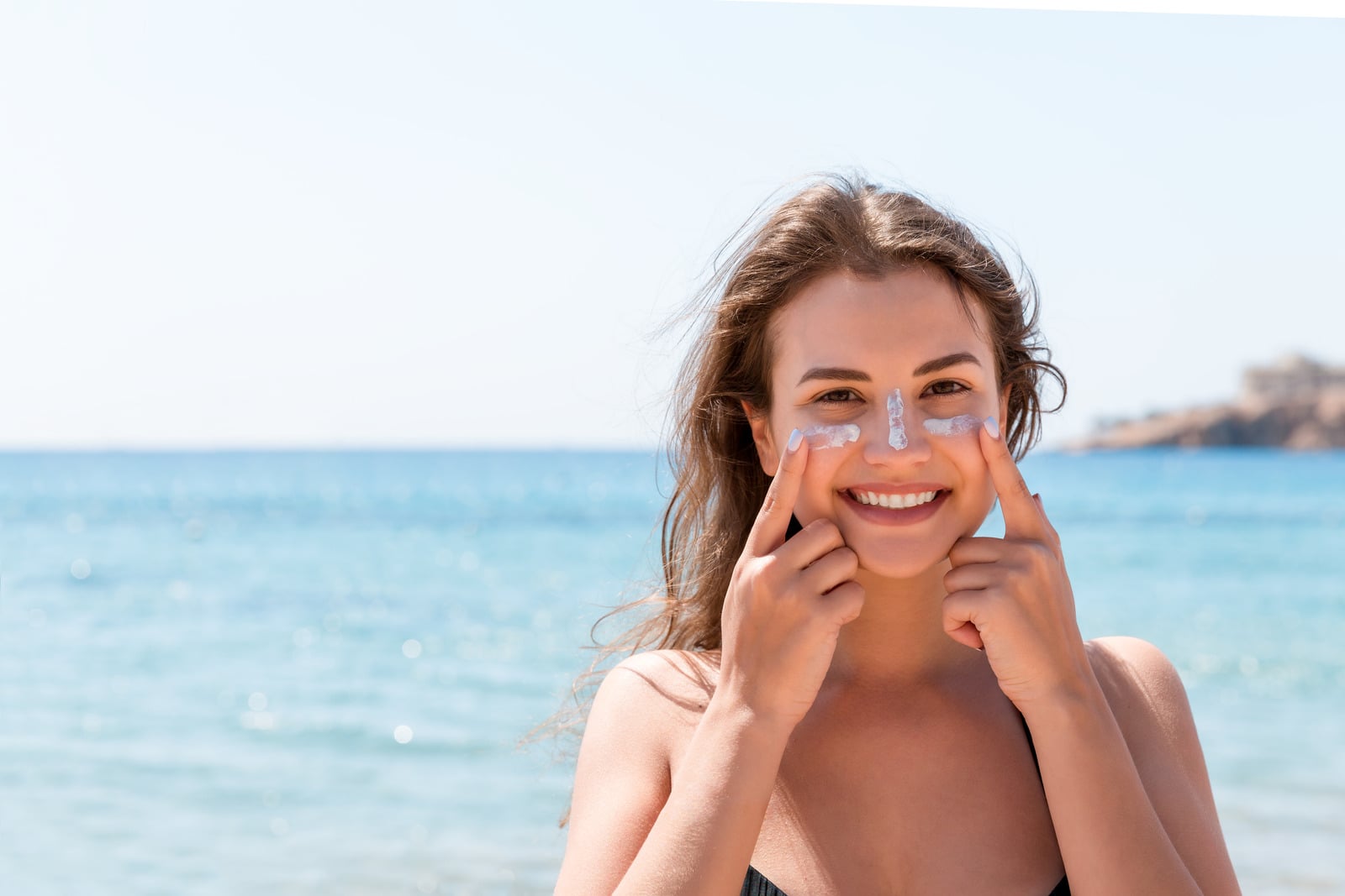 Ragazza applica la crema solare sul viso davanti al mare